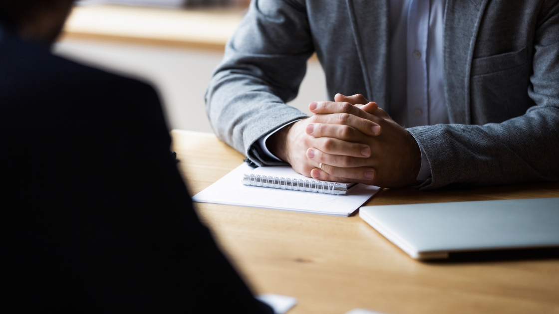 A businessman sits at a desk, his hands folded.